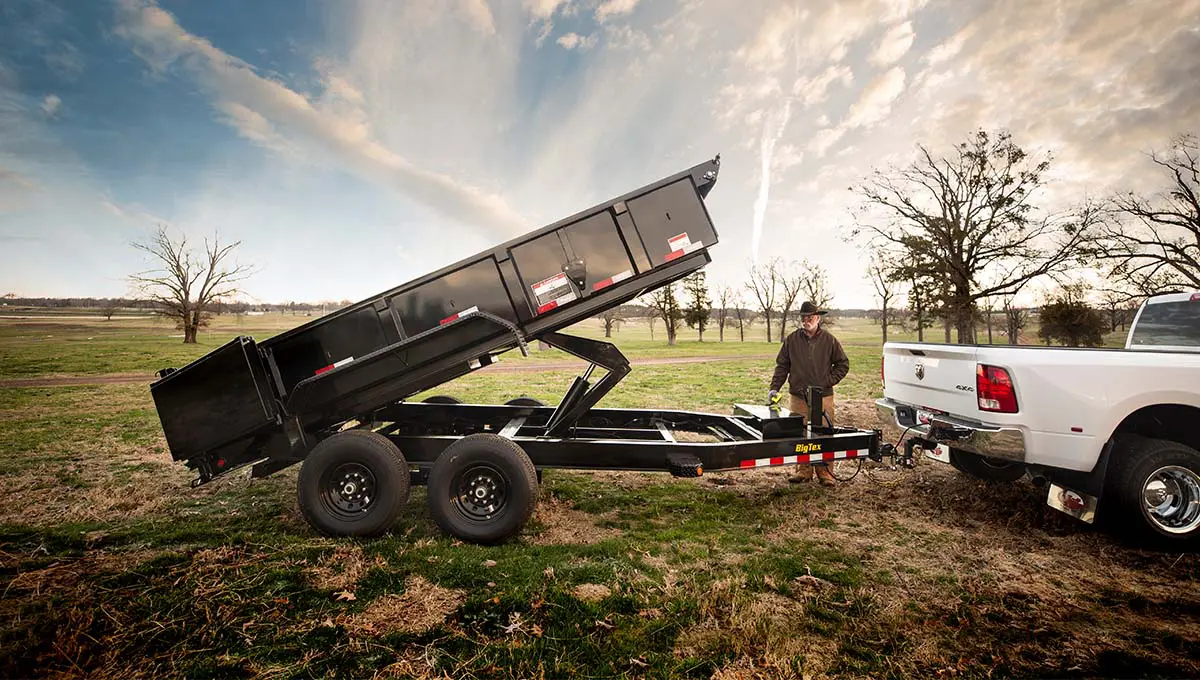 a man is standing next to a ram truck with a 14lp commercial grade dump trailer attached to it