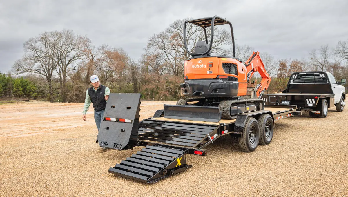 a man is loading a small orange kubota excavator on a trailer