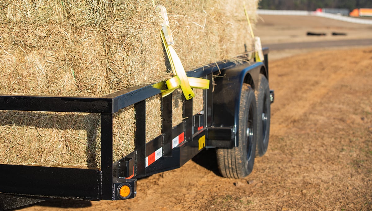 a 10pi utility trailer is loaded with hay and has a yellow safety strap