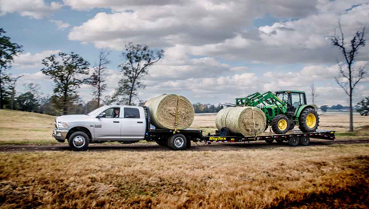 a ram truck is pulling a 14ph hydraulic dovetail trailer with bales of hay on it