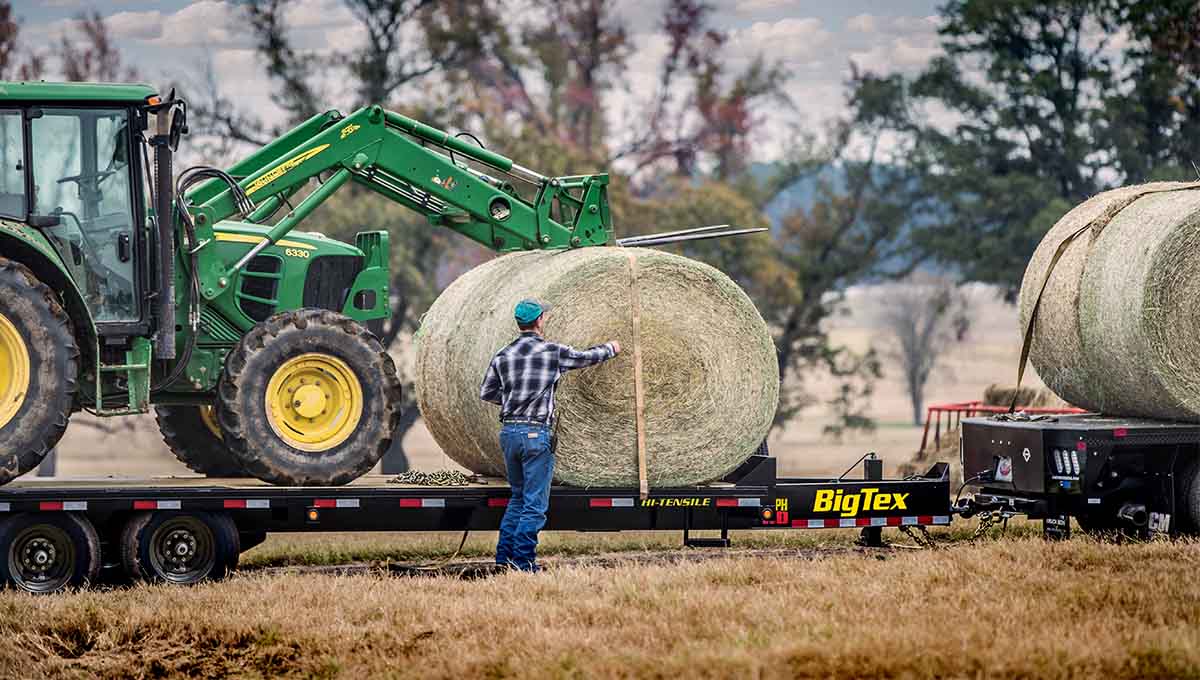 a man measures a bale of hay on a big tex 14ph gooseneck trailer