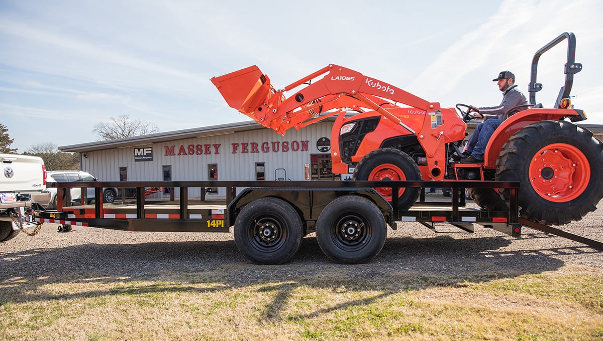 a man is driving a kubota tractor on a 14PI tube top utility trailer