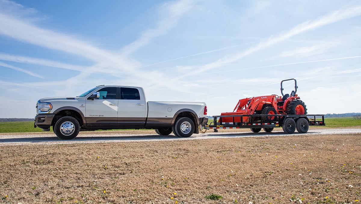a white ram truck is towing a red kubota tractor with a 14pi utility trailer
