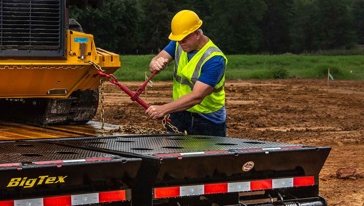 a man is working on a big tex 22ph hydraulic dovetail gooseneck trailer