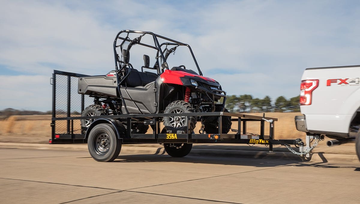 a white truck is towing a 35sa utility trailer with a red atv on it