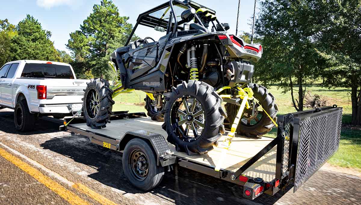a white ford truck is towing a polaris atv on a trailer
