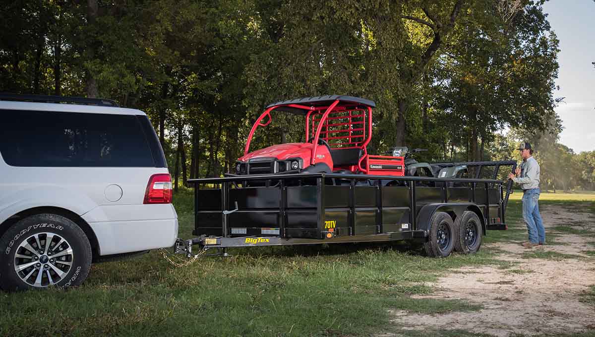 a white suv is towing a 70tv vanguard trailer with a red tractor on it