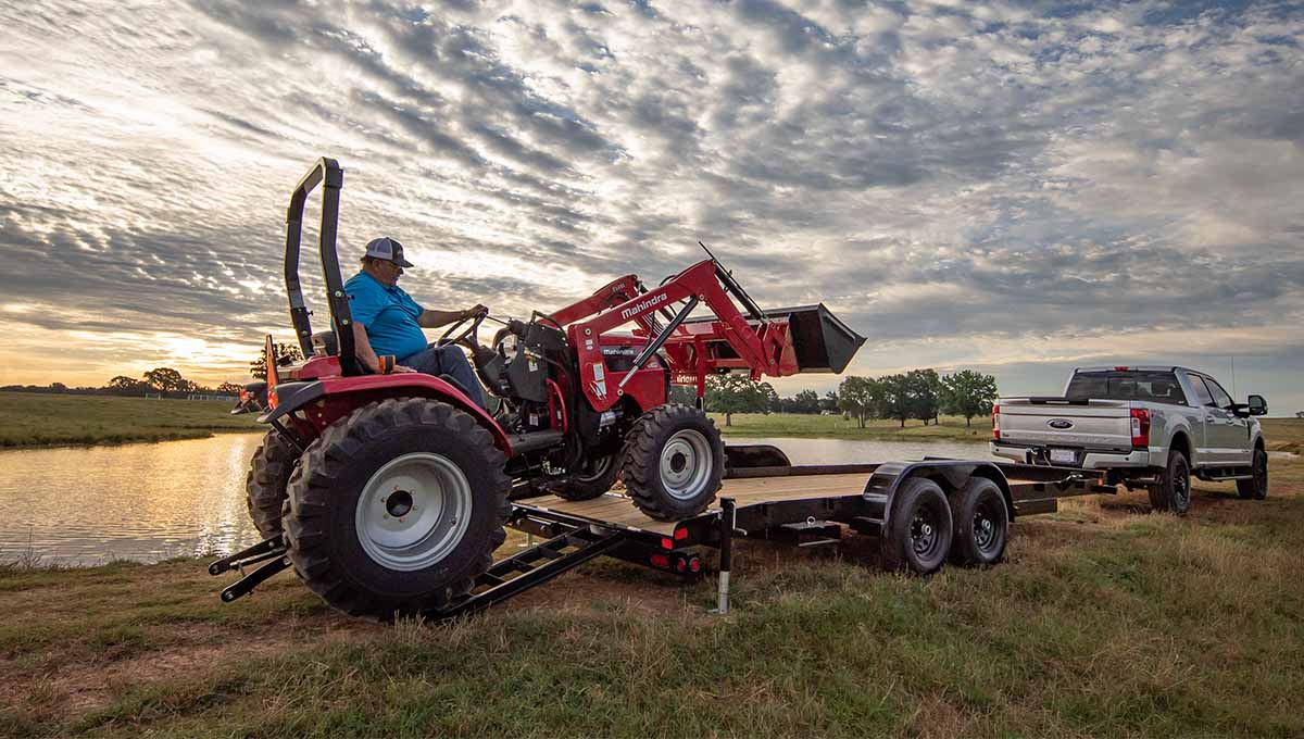 a ford truck is towing a tractor on a 10ch car hauler trailer