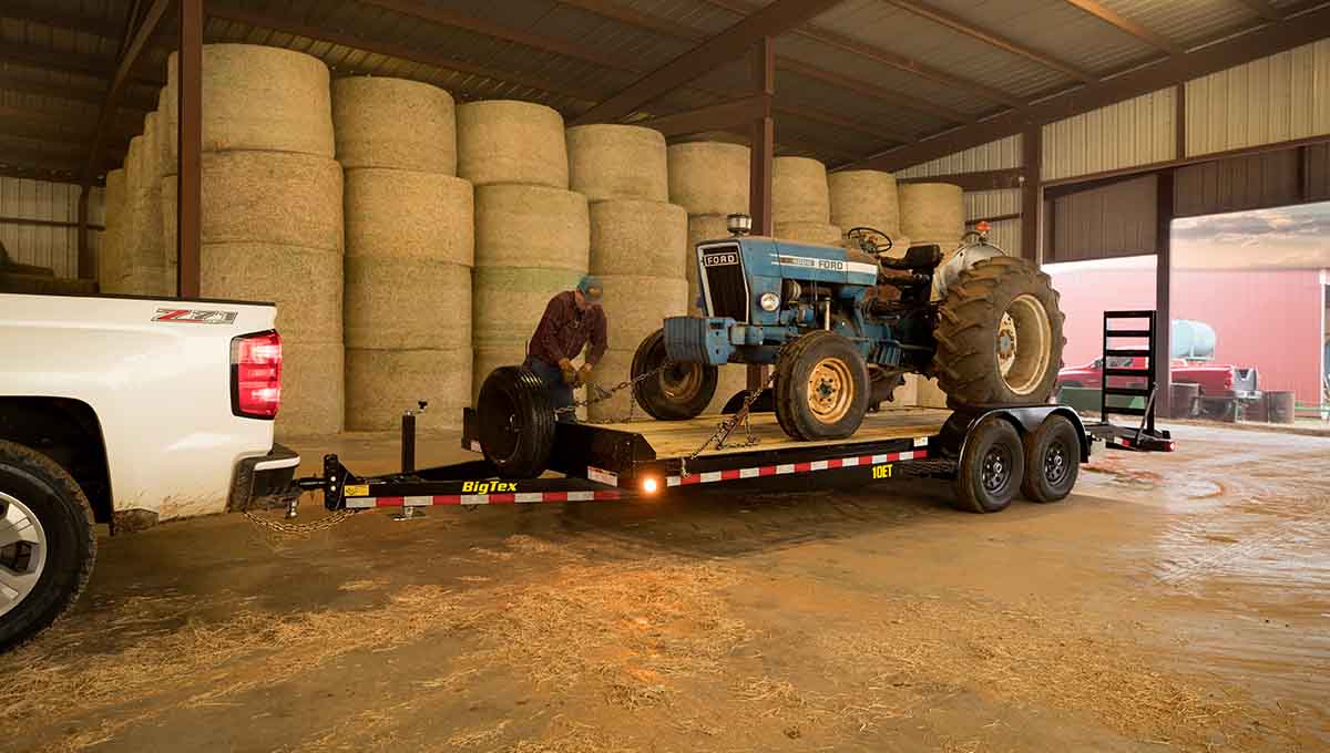 a ford tractor is being towed by a 10et equipment big tex trailer