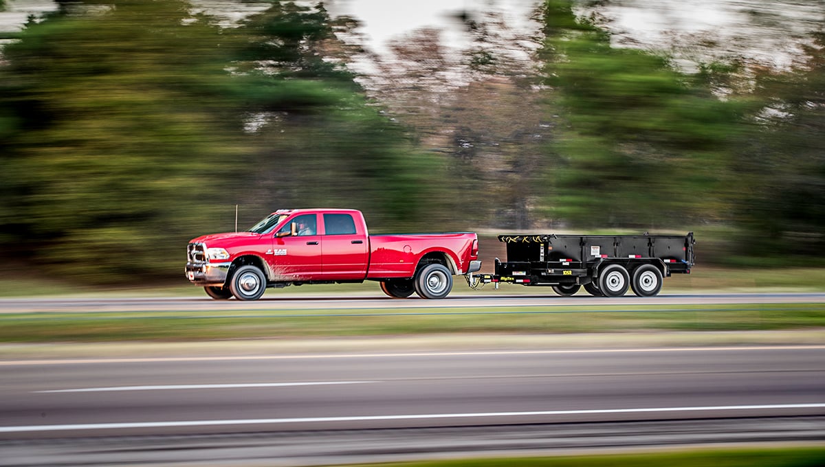 a red ram truck is pulling a 10sr commercial dump trailer on a highway