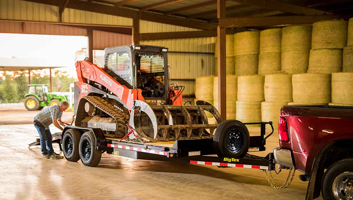 a red truck is pulling a 14et equipment hauler trailer with a kubota skid steer on it