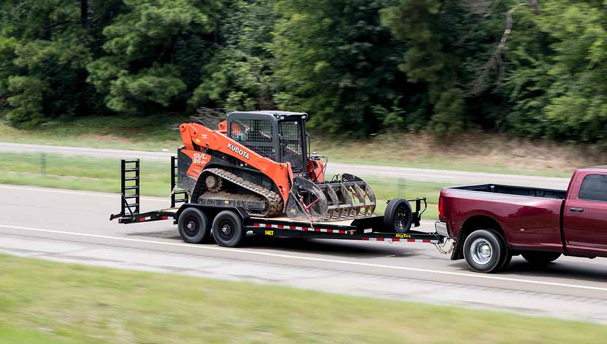 a red truck is pulling a 14et equipment hauler trailer with a kubota skid steer on it