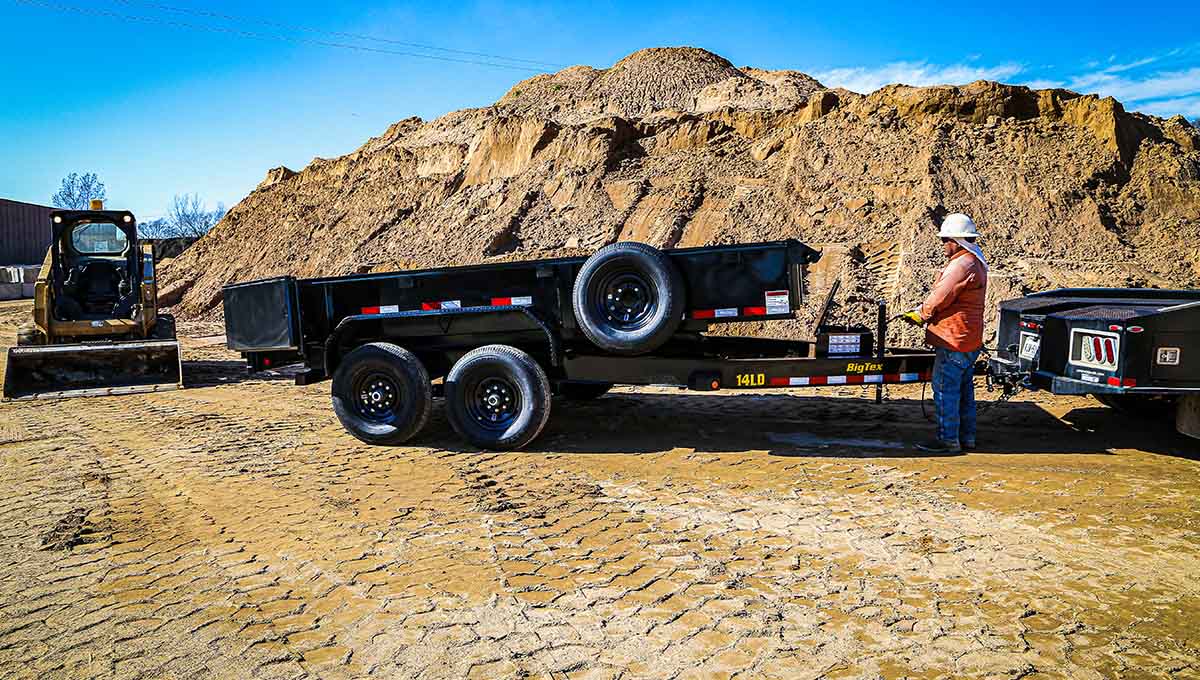 a man is standing next to a dump trailer that says 'm&m' on the side