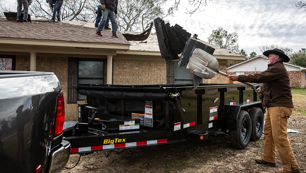 a man is loading a dumpster on a 14lp commercial grade dump big tex trailer
