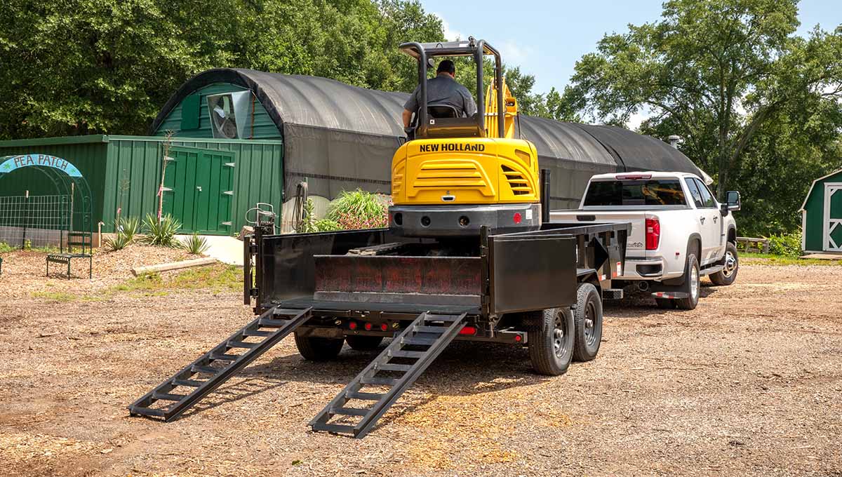 a yellow new holland excavator is being towed by a 14td commerical grade dump trailer