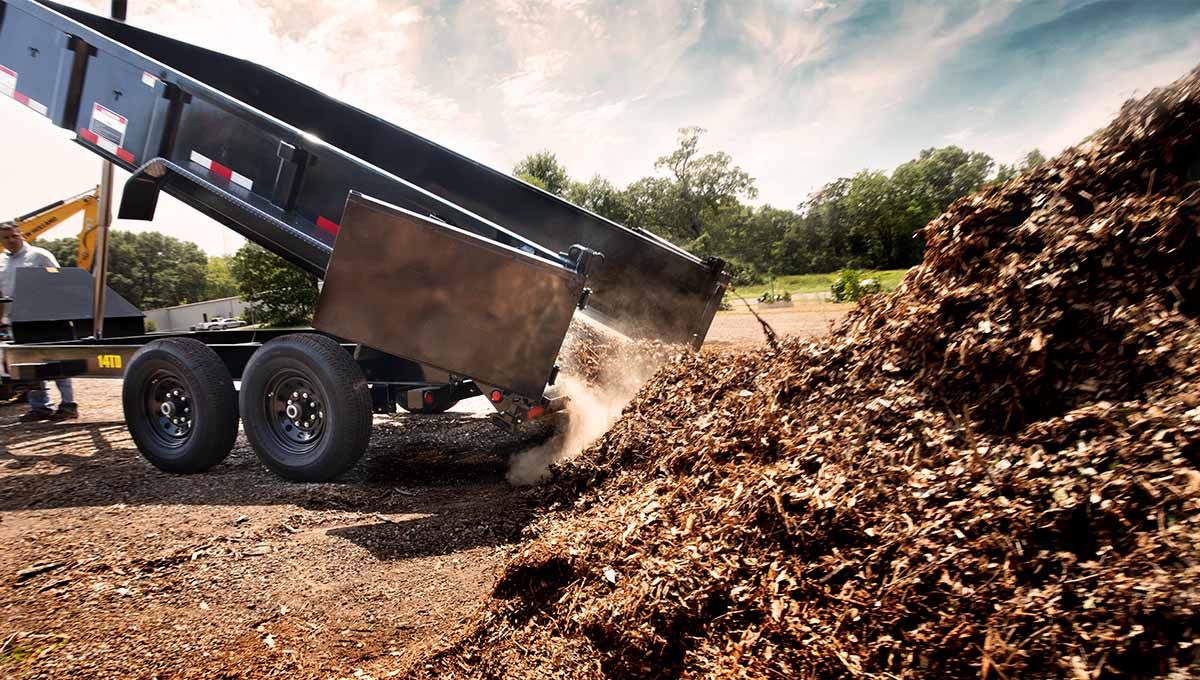 a 14TD commercial grade dump trailer is dumping a pile of wood chips