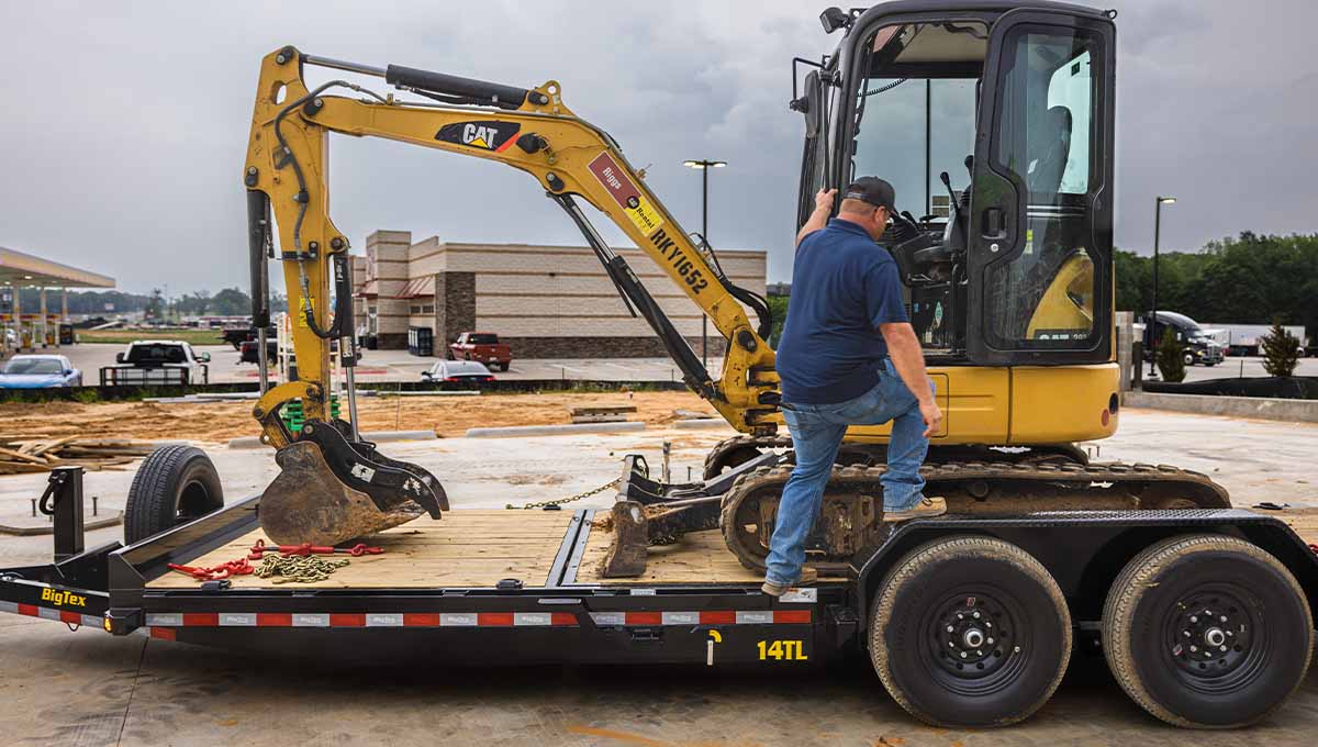 a man standing on a 14tl trailer next to a cat excavator