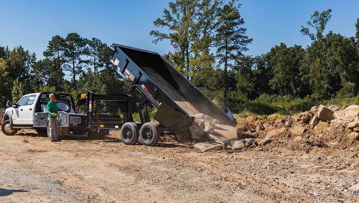 a man stands next to a dump truck that has a 16gx commercial grade dump trailer attached to it