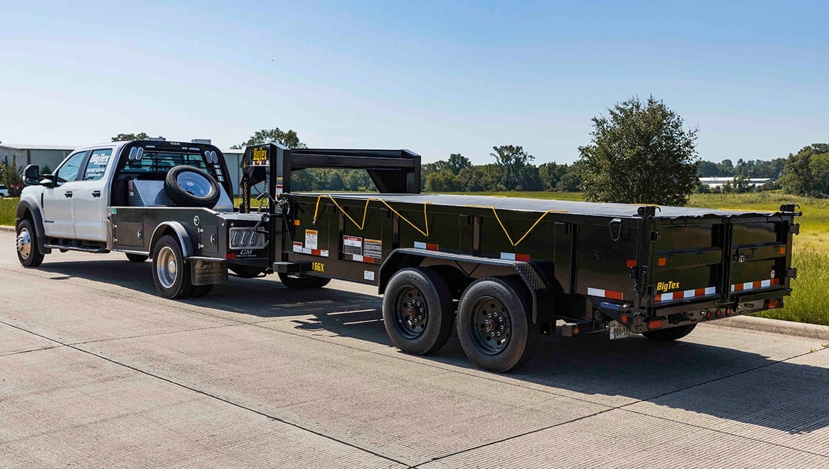 a 16gx big tex dump trailer is being towed by a white truck