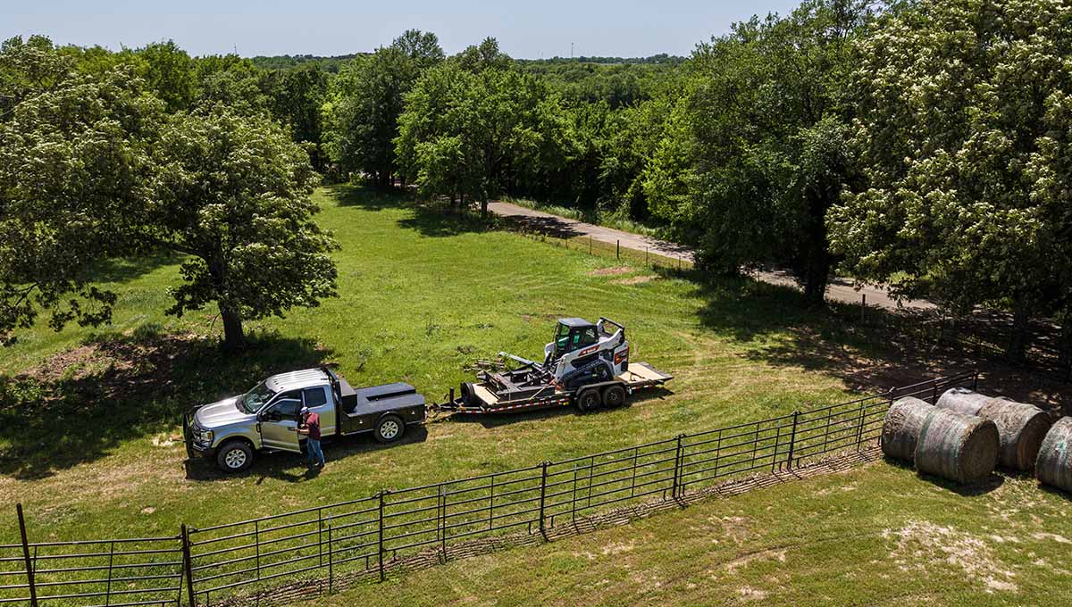 a white truck is parked next to a 16tl trailer with a bobcat on it