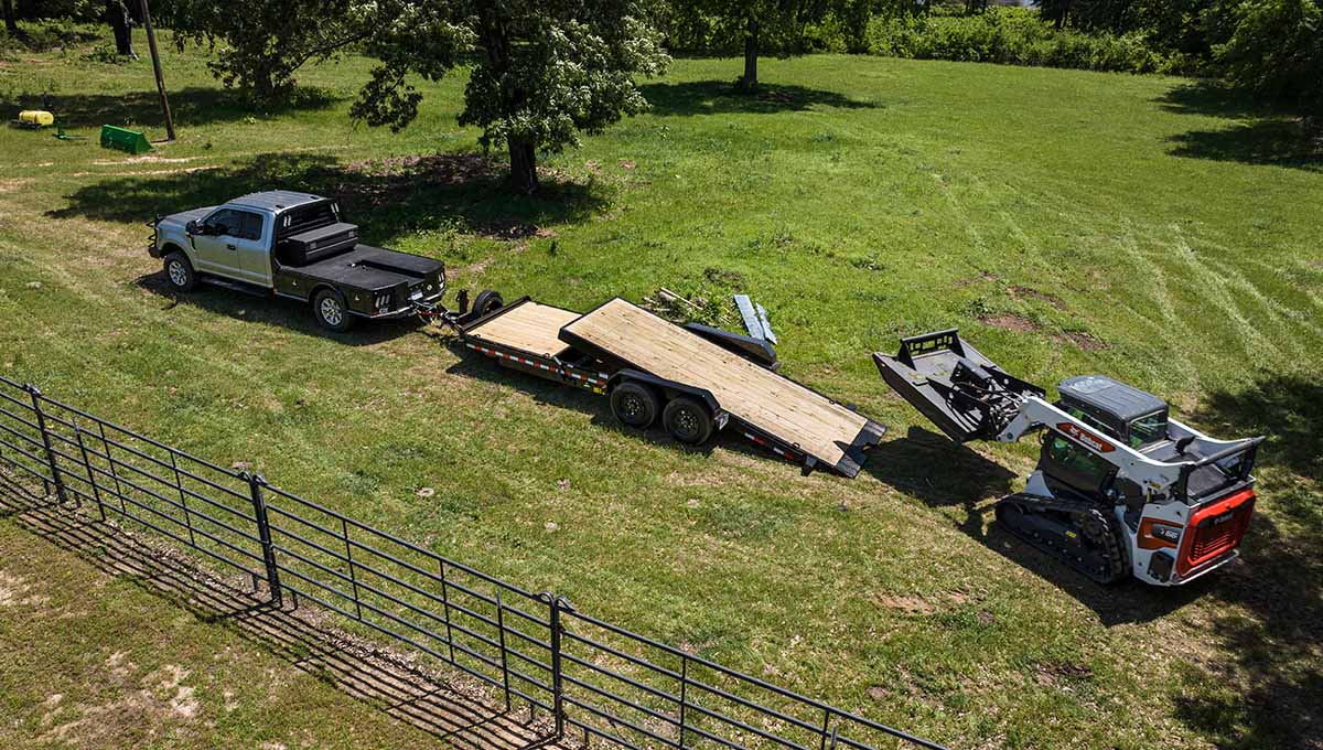 a bobcat is pulling a 16tl flatbed trailer in a grassy field