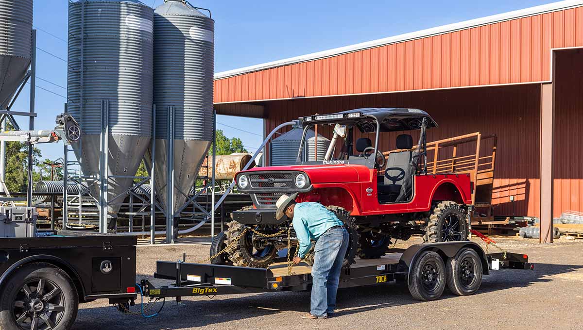 a man is working on a red jeep on a 70CH wood deck car hauler trailer that says big tex