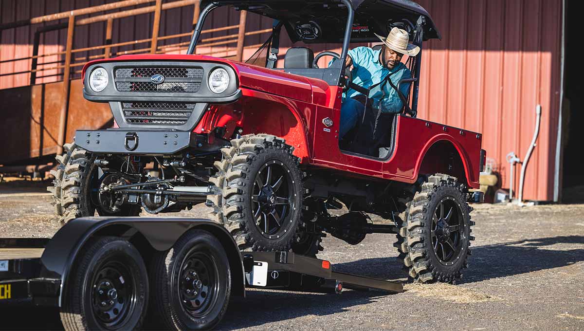 a man in a cowboy hat is driving a red jeep on a car hauler trailer