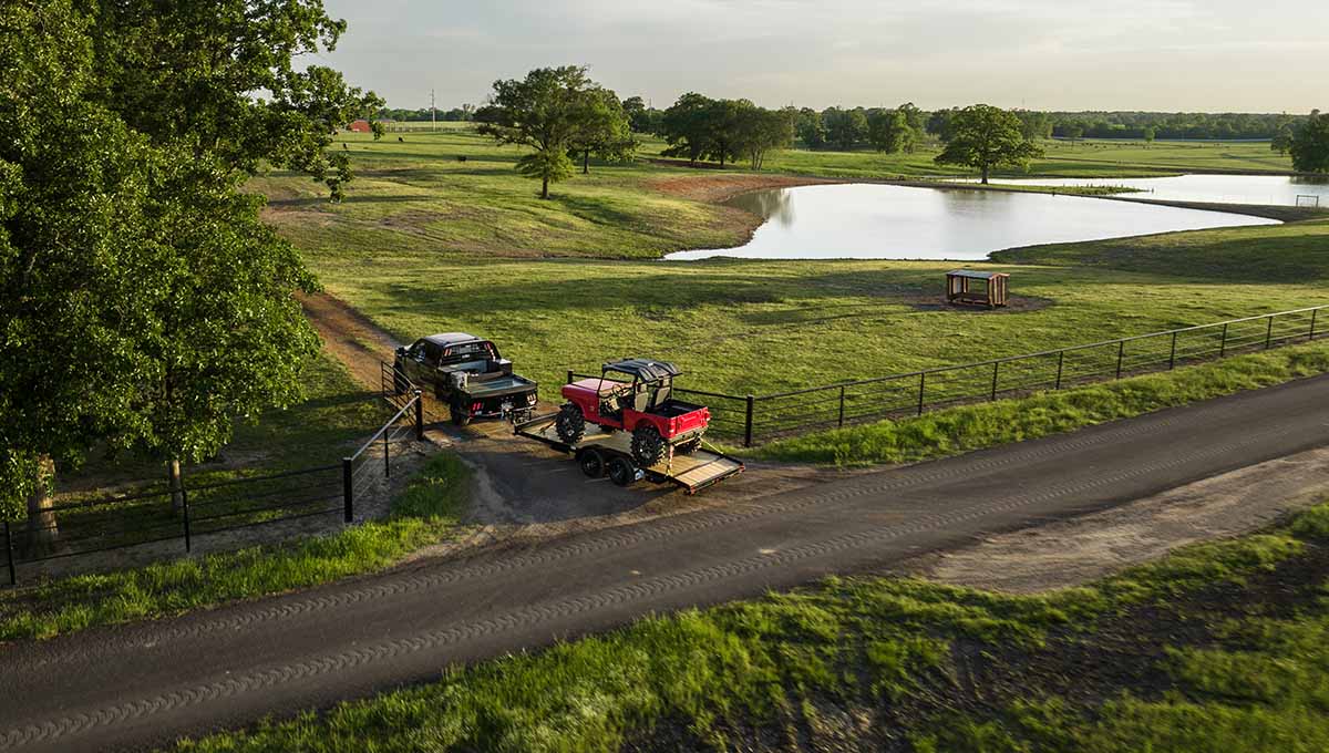 two trucks are parked on a dirt road near a lake