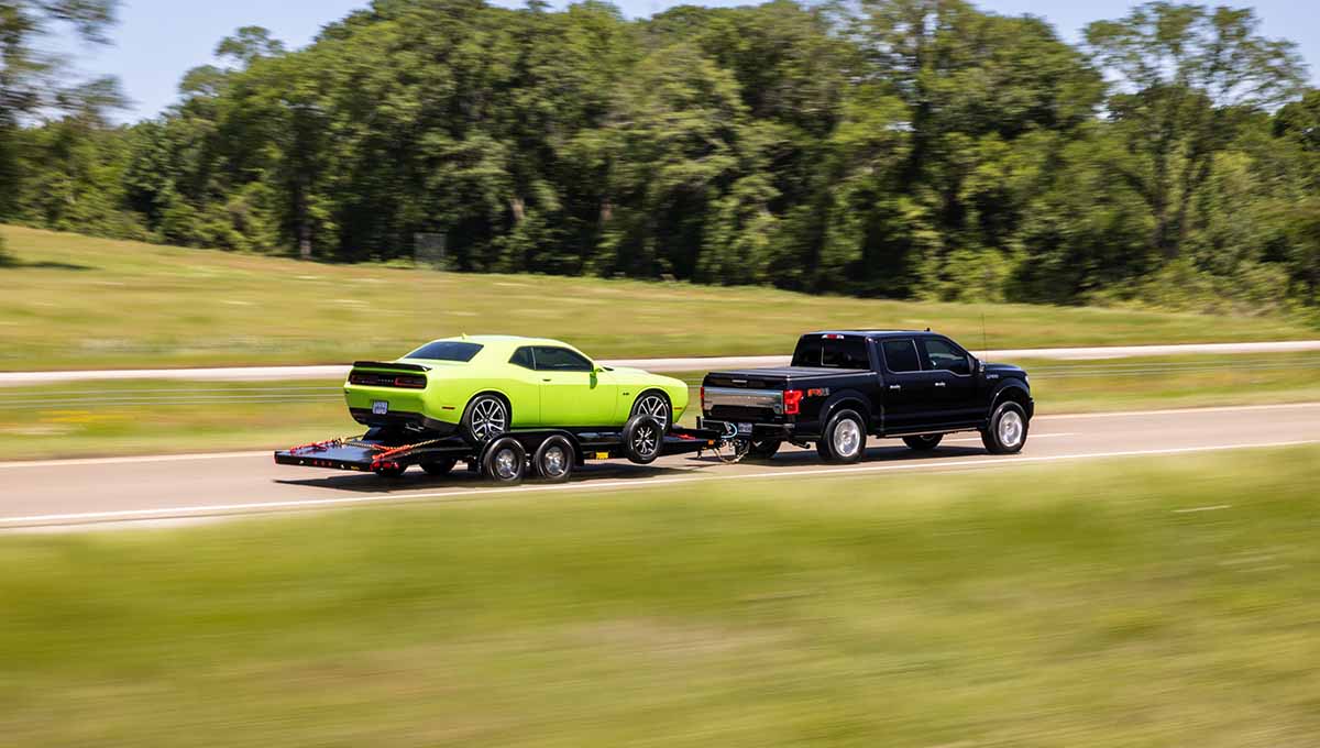 a black truck is towing a green dodge challenger on a 70dm car hauler trailer