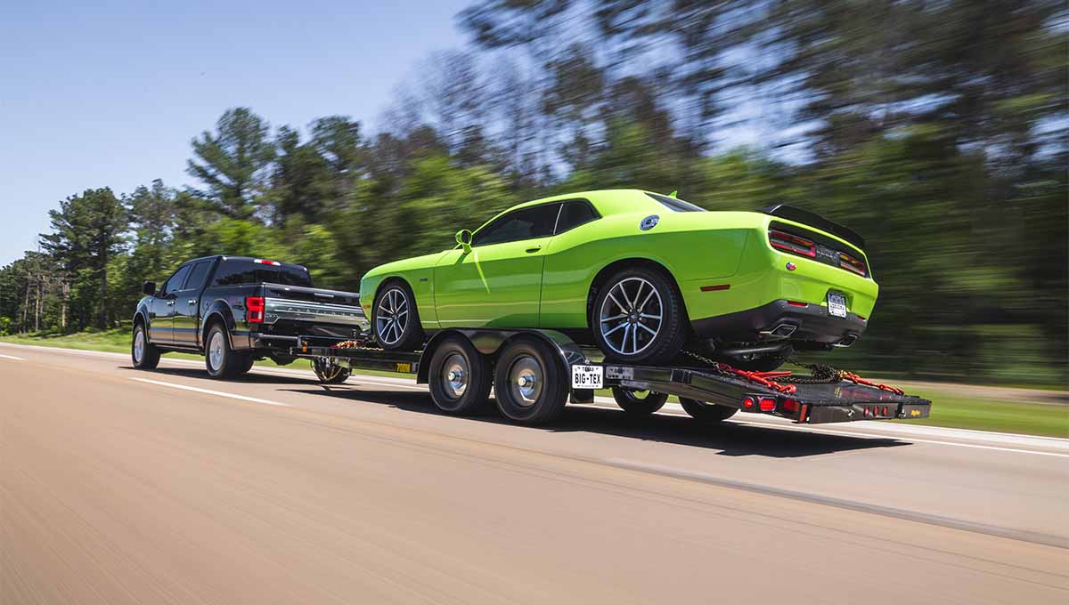 a truck is towing a green dodge challenger on a 70dm car hauler trailer