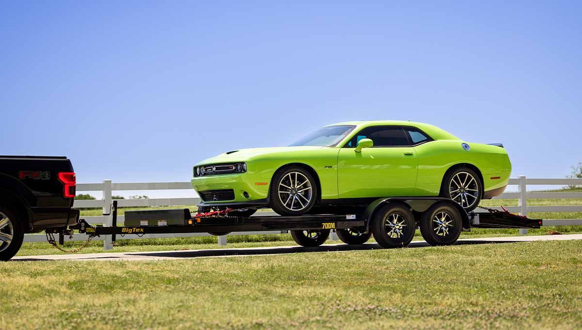 a green dodge challenger is being towed by a big tire trailer