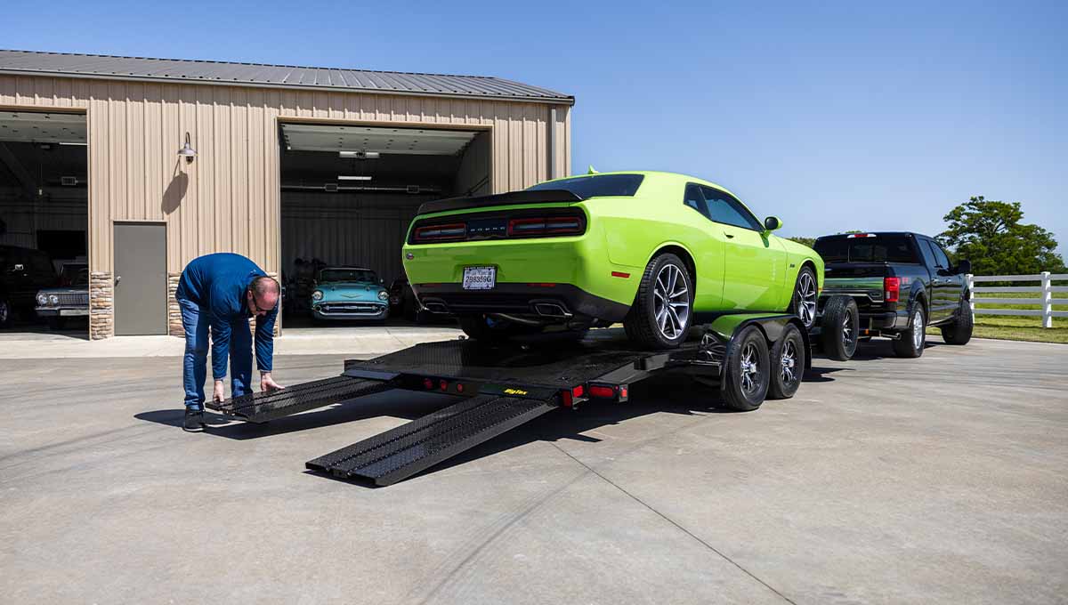 a green dodge challenger is on a 70dm car hauler trailer in front of a garage