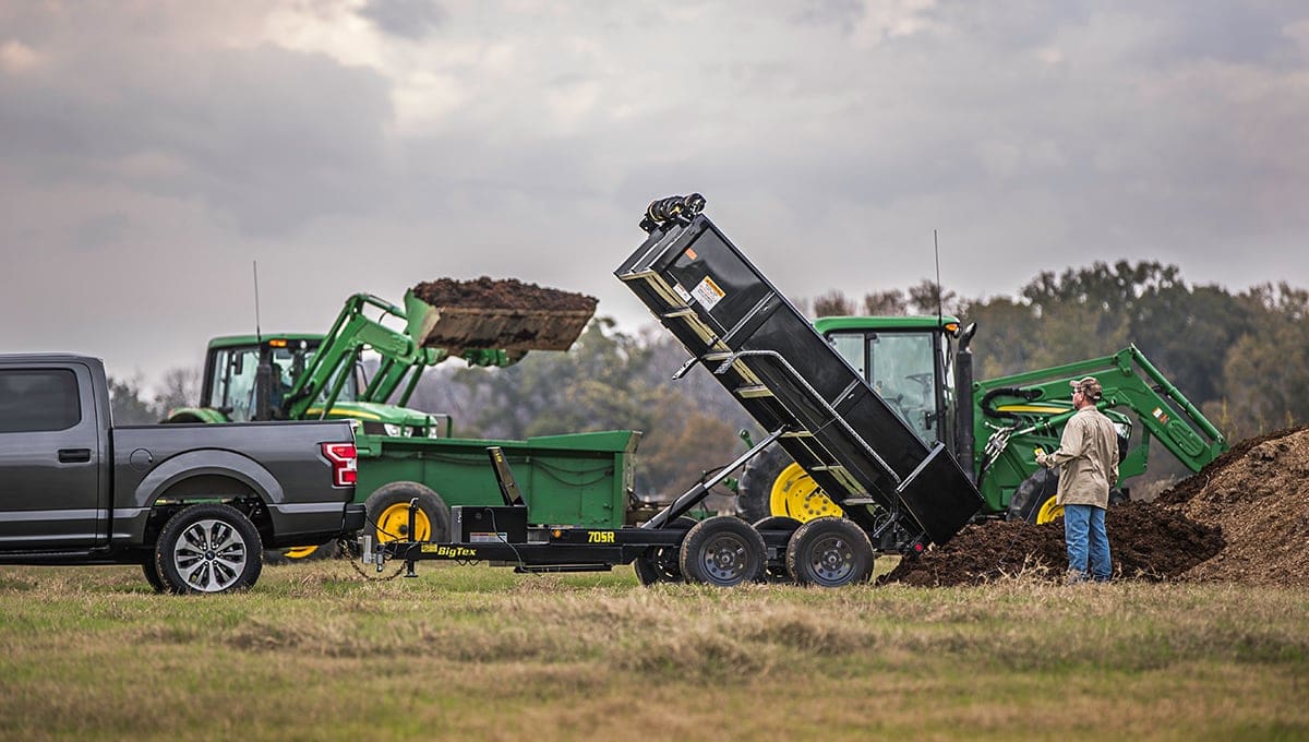 a john deere tractor is loading dirt into a big tex 70sr compact dump trailer