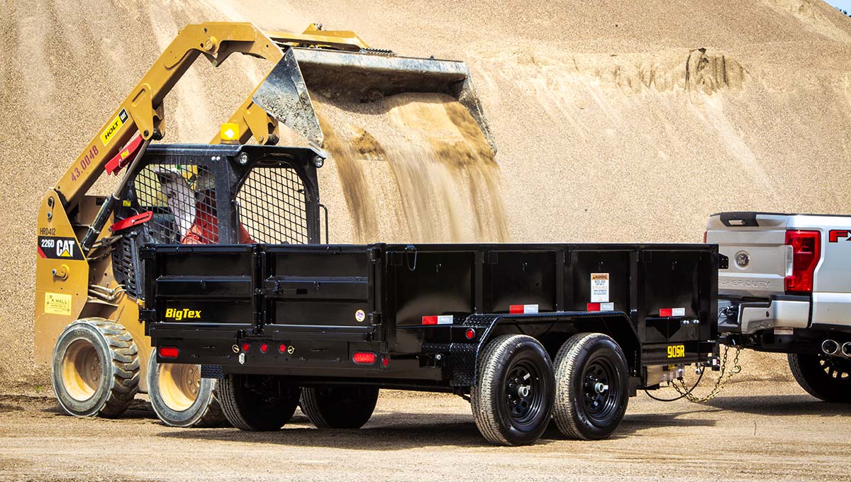 a big tex 90sr dump trailer is being pulled by a cat skid steer