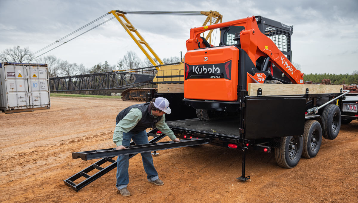 a man is loading a kubota skid steer into a 14xd trailer