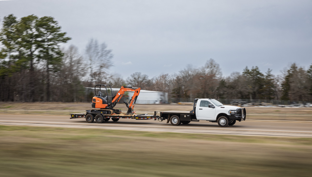 a white truck is pulling a small orange excavator on a eh5 trailer