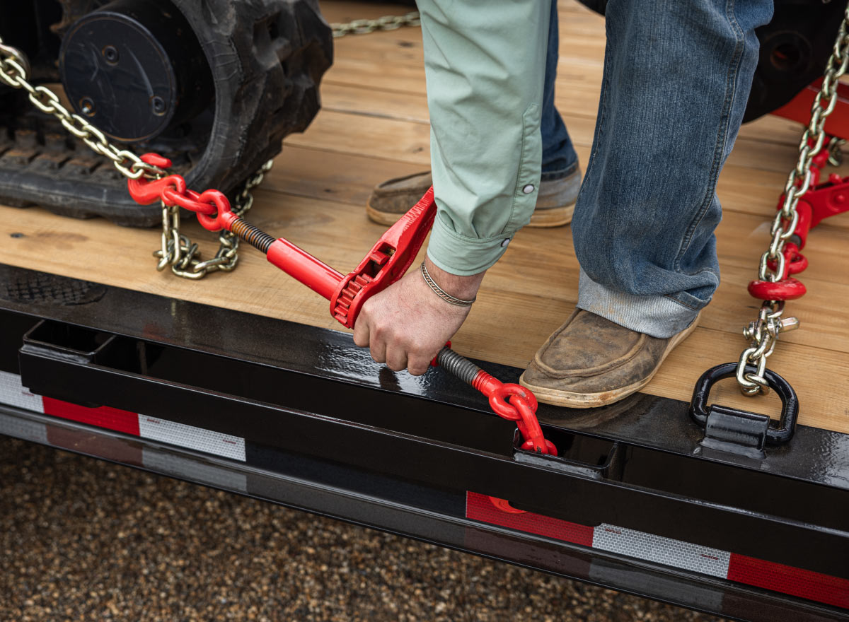 a man is attaching chains to a trailer with a tool