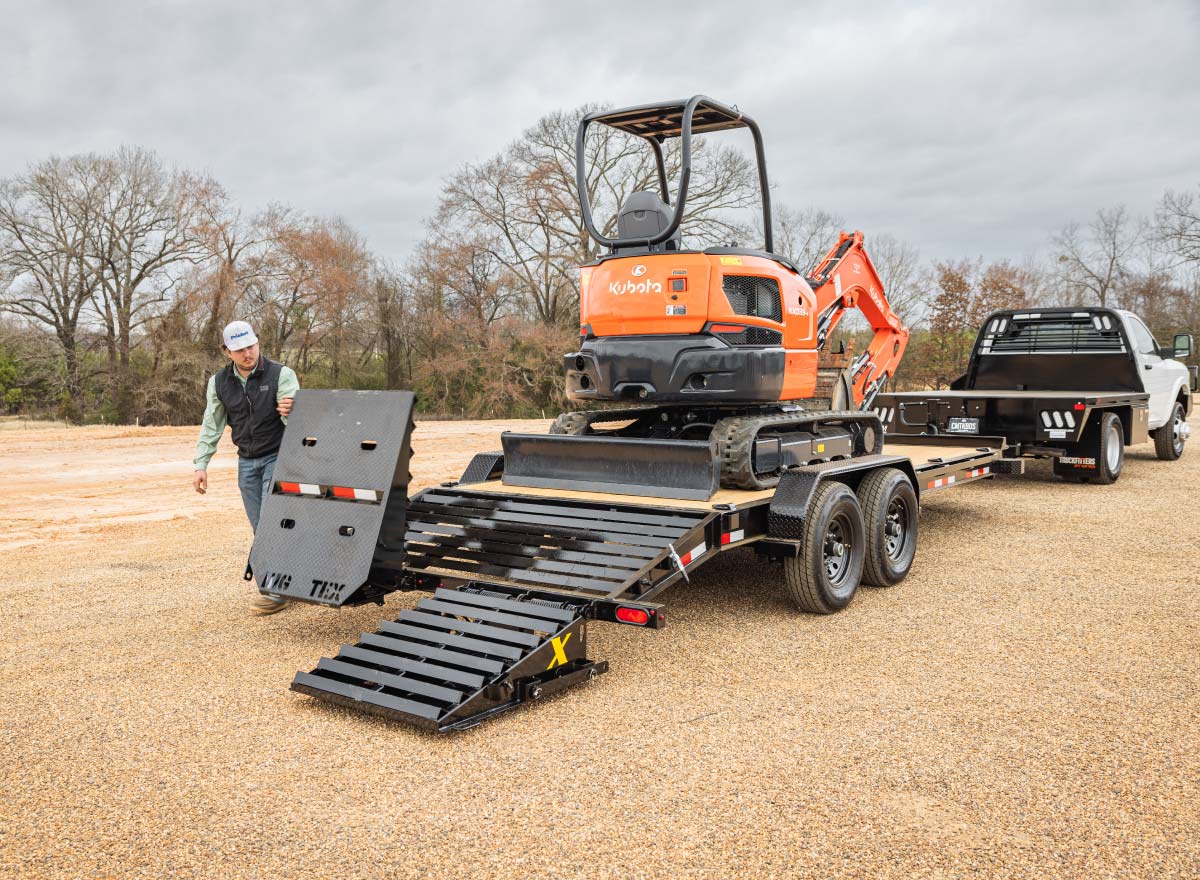 a man is loading a small orange kubota excavator on a trailer
